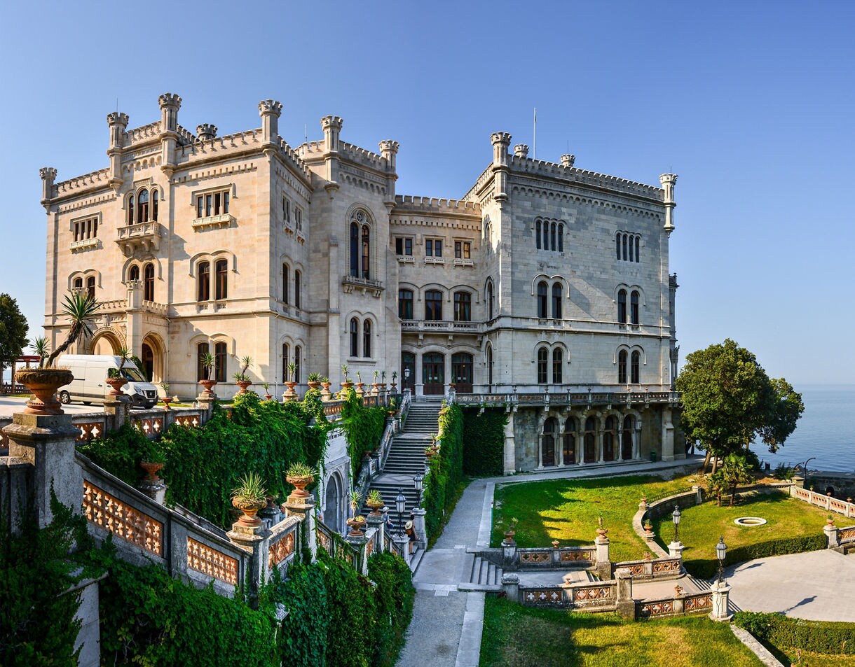 Miramare Castle perched above the Adriatic with ivy-covered stairways, arched windows and bright green lawns surrounding the estate.