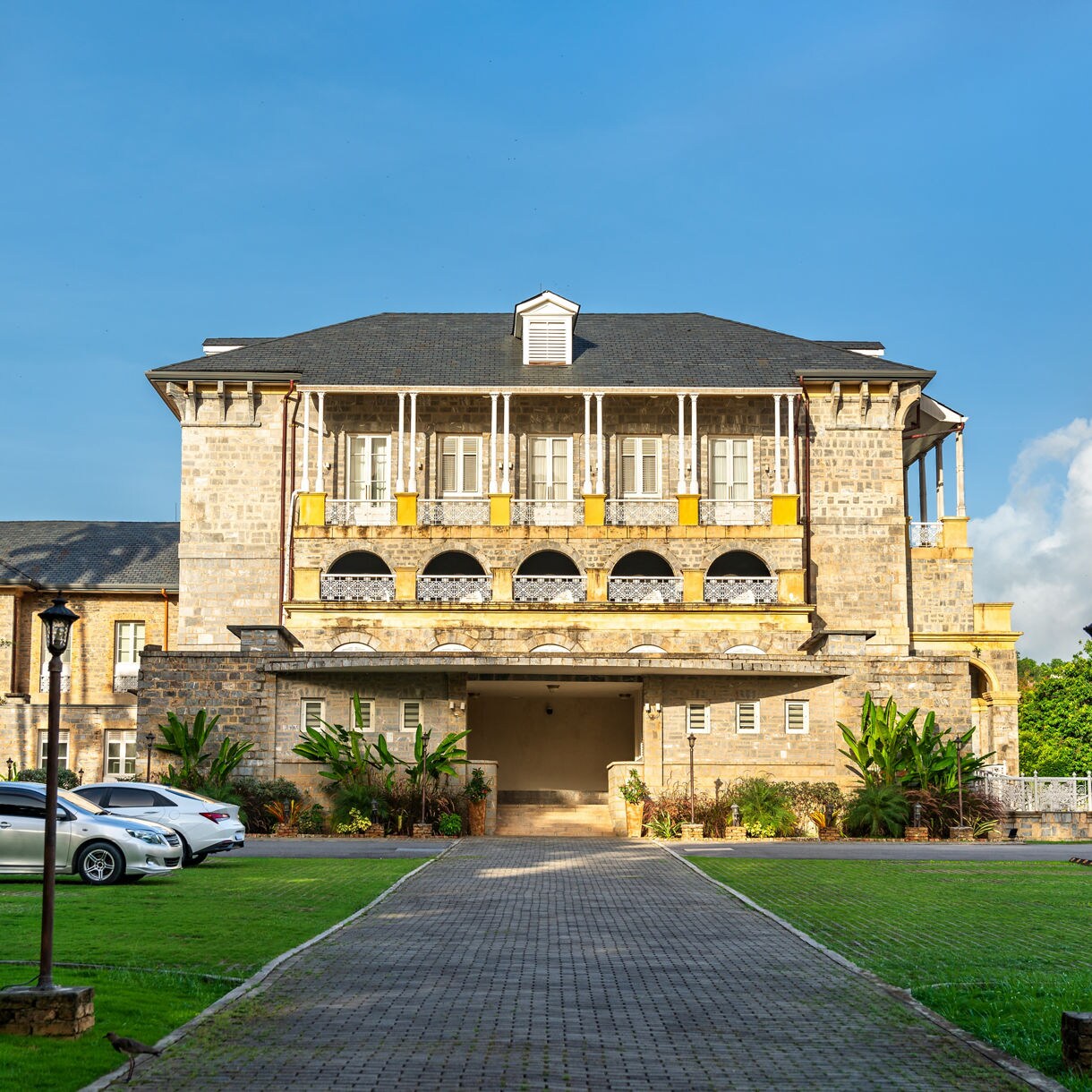 A historic stone building with colonial-style balconies and arches, surrounded by lush greenery in Trinidad’s Botanical Gardens.