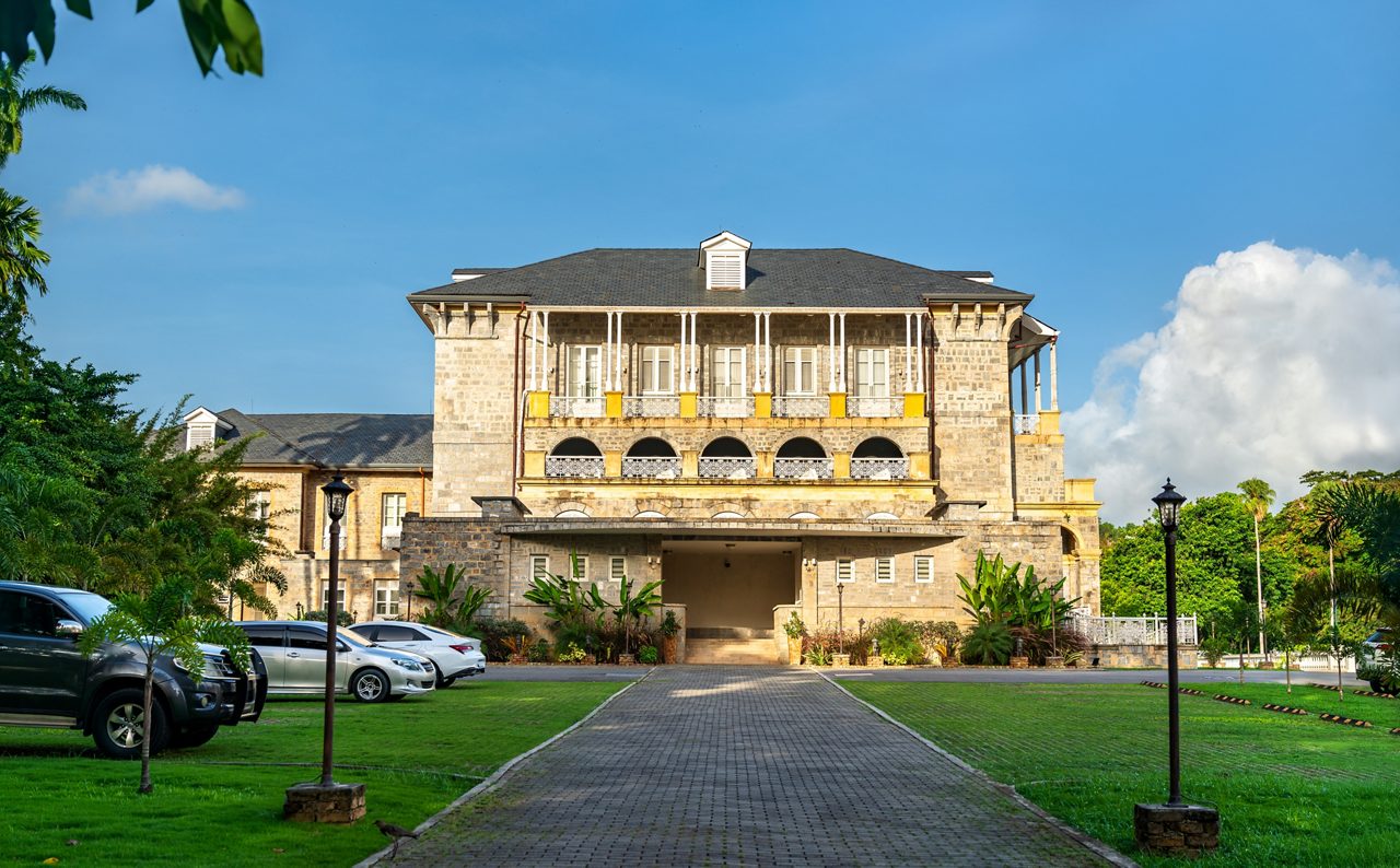 A historic stone building with colonial-style balconies and arches, surrounded by lush greenery in Trinidad’s Botanical Gardens.