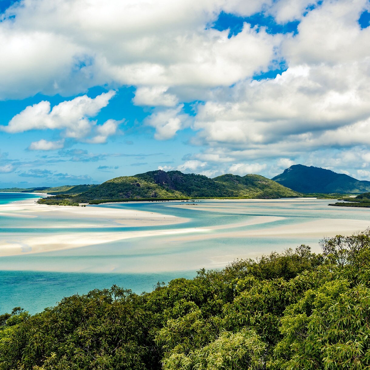 View of Hill Inlet’s curving sandbars and turquoise waters framed by lush green hills under a bright sky.