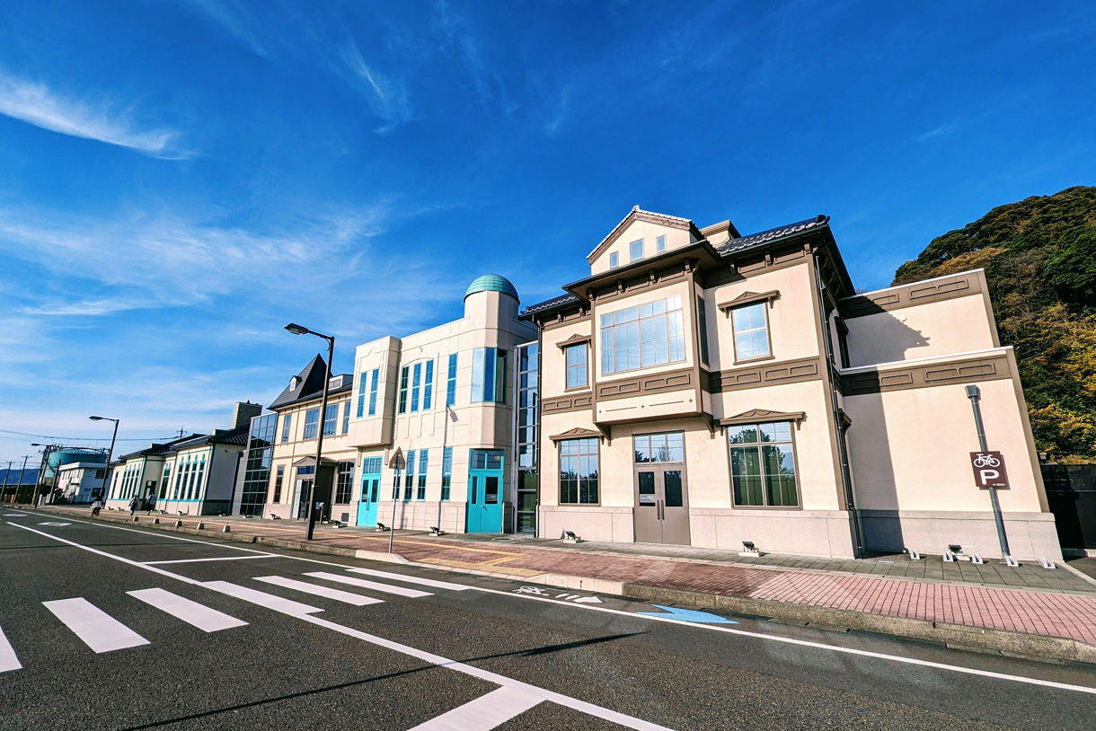 Wide-angle view of the Tsuruga Museum buildings, featuring restored Western-style architecture with pastel accents under a vivid blue sky.