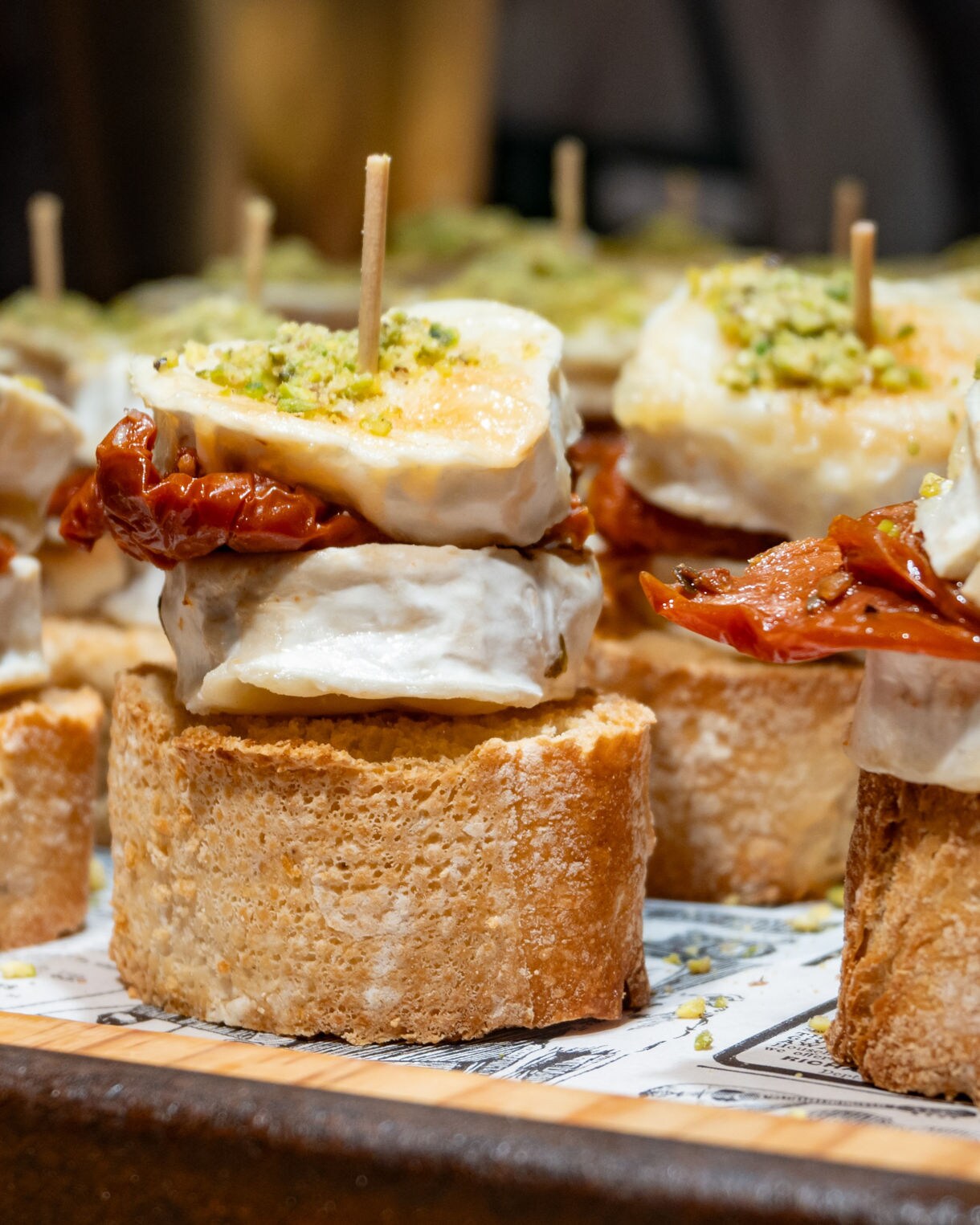 Close-up of traditional Basque pintxos made with bread, cheese and sun-dried tomatoes, garnished with crushed pistachios and secured with toothpicks.