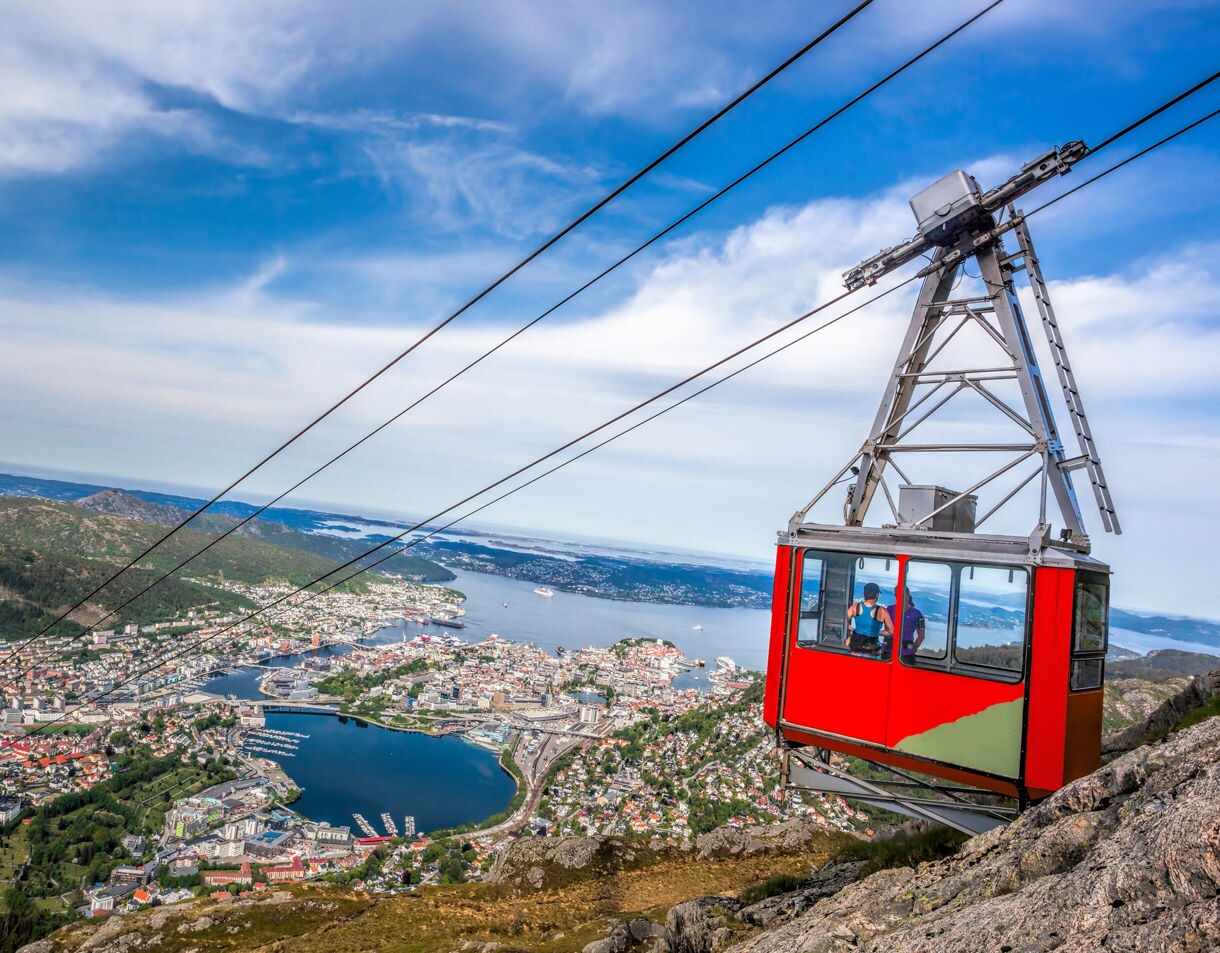 Red Ulriken cable car ascending a steep mountain slope with panoramic views of Bergen, its harbor and surrounding islands.