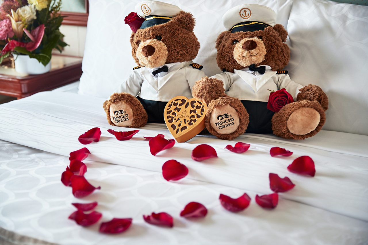 stuffed bears on a bed with rose petals in the shape of a heart