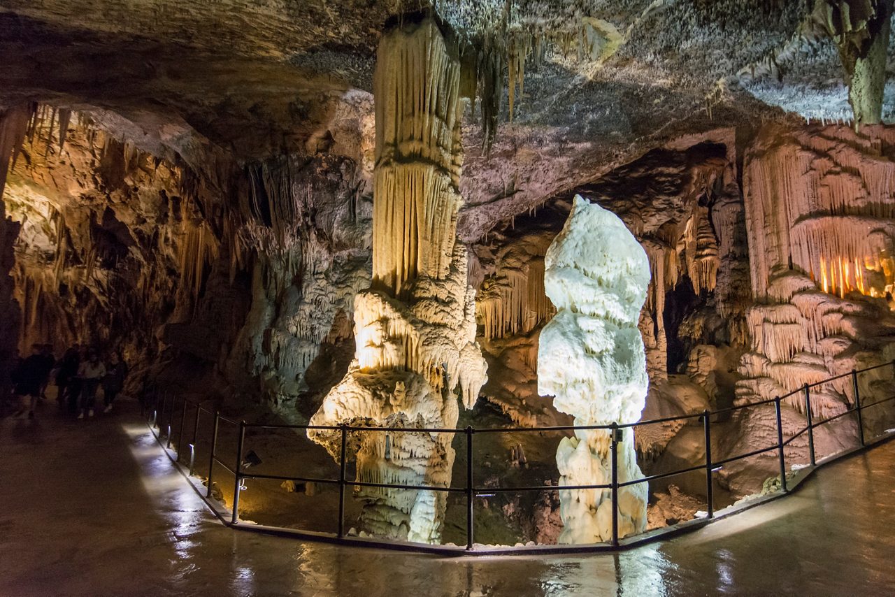 Illuminated limestone formations in Postojna Cave, Slovenia, featuring massive stalactites, stalagmites, and columns with a walkway for visitors.