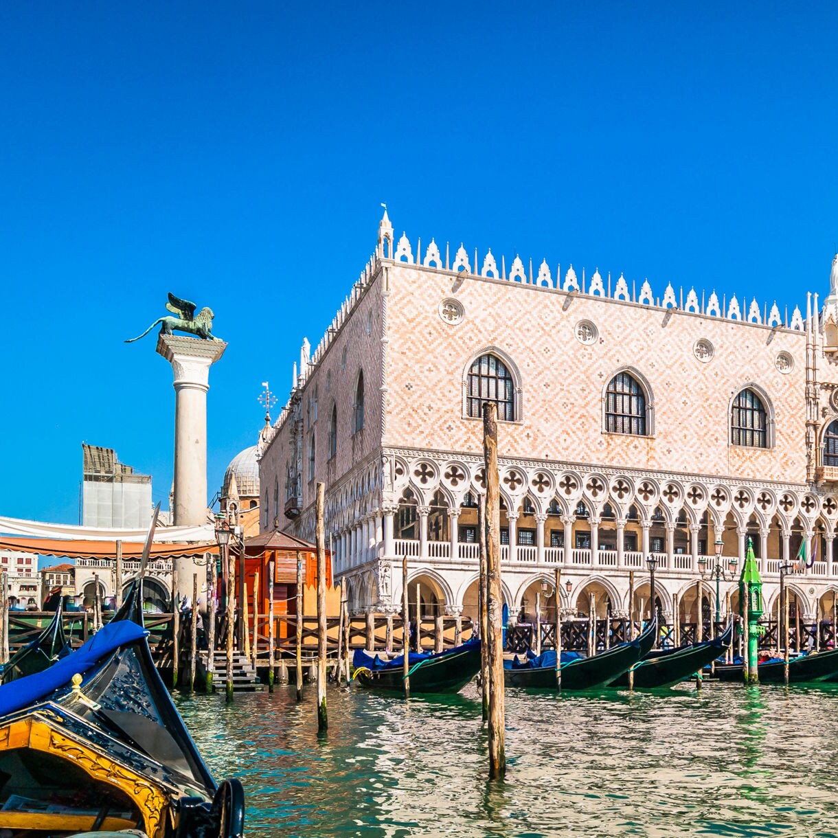 Boats docked in a marina below towering cliffs, topped with colorful villas in Sorrento at sunset.