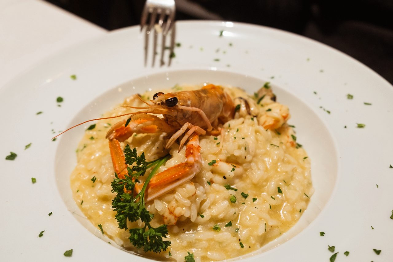Plate of seafood risotto topped with a whole prawn and garnished with parsley.