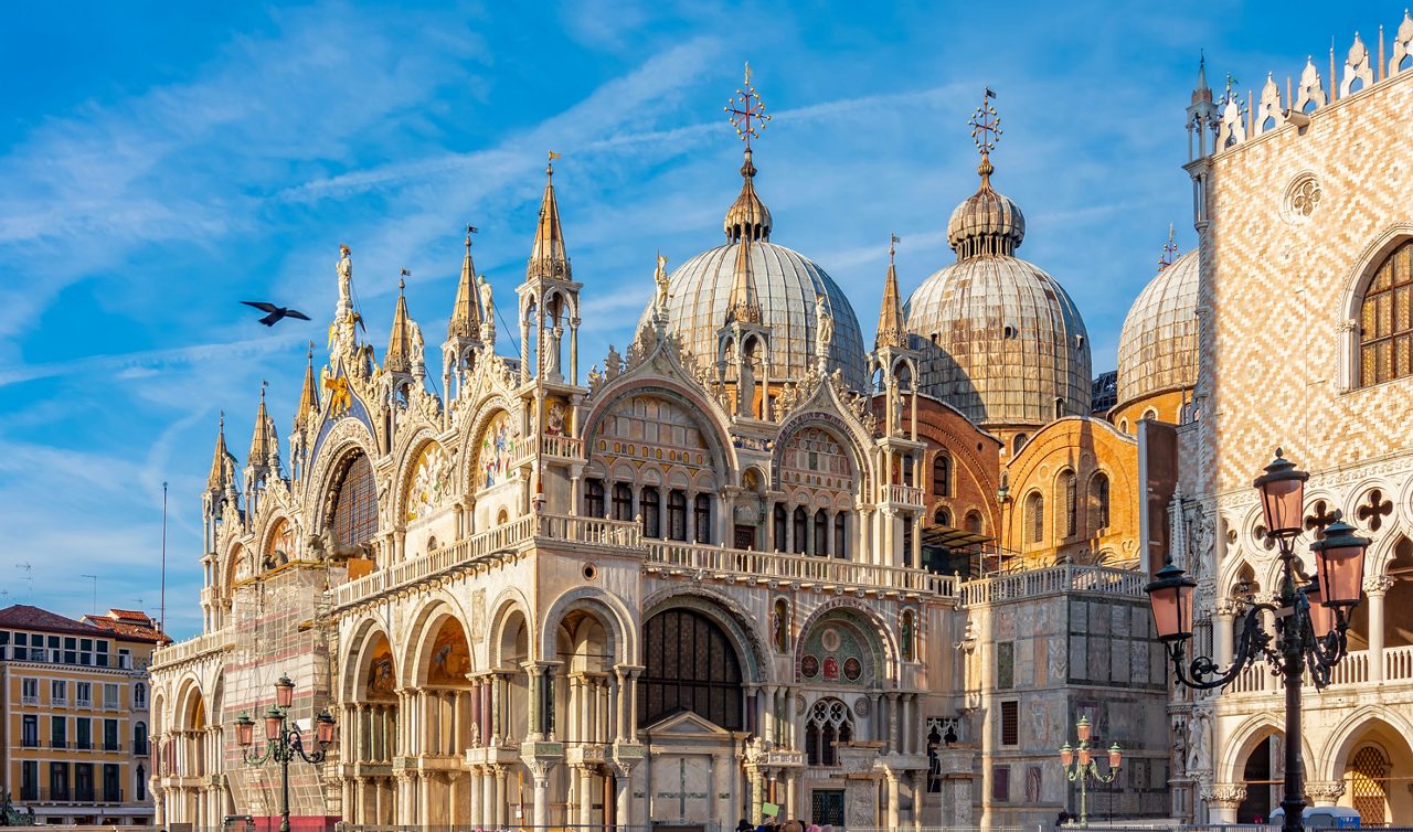 Ornate façade and domes of St. Mark’s Basilica in Venice under a bright blue sky.