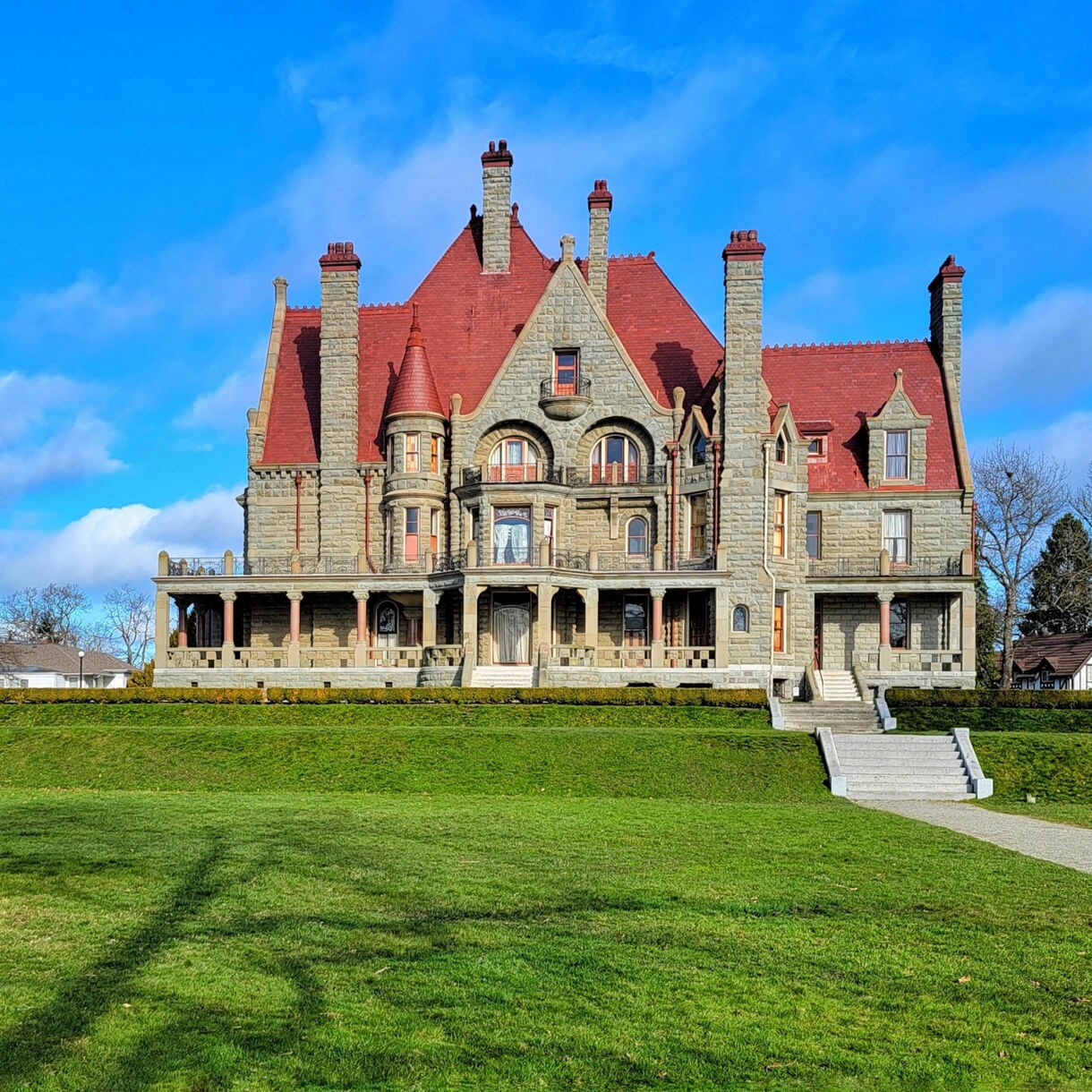 The imposing Craigdarroch Castle in Victoria, British Columbia, with its red-tiled roof, towering stone structure and expansive green lawn leading up to the grand entrance.