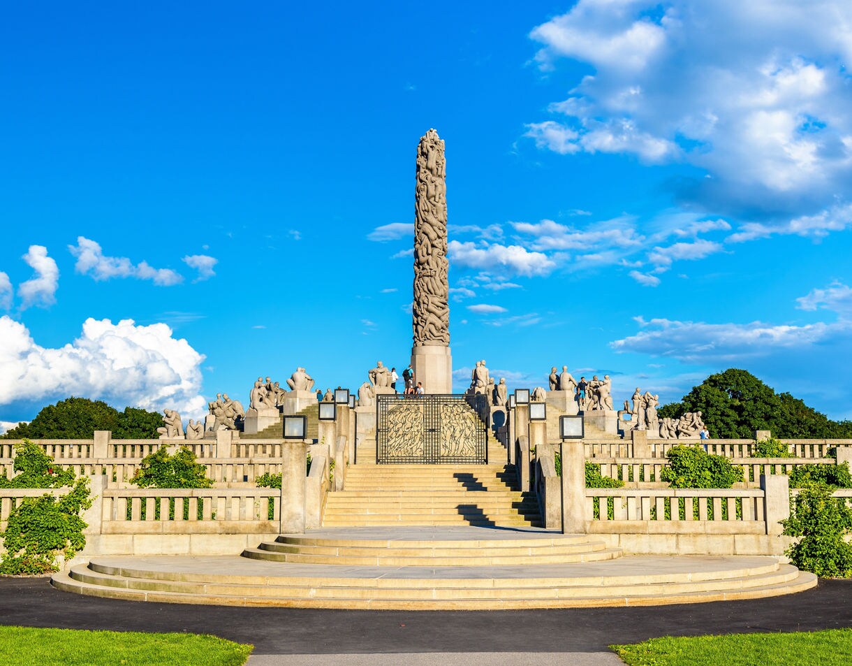 Vigeland Sculpture Park in Oslo, Norway, featuring the Monolith column surrounded by stone statues on terraced steps under a bright blue sky.