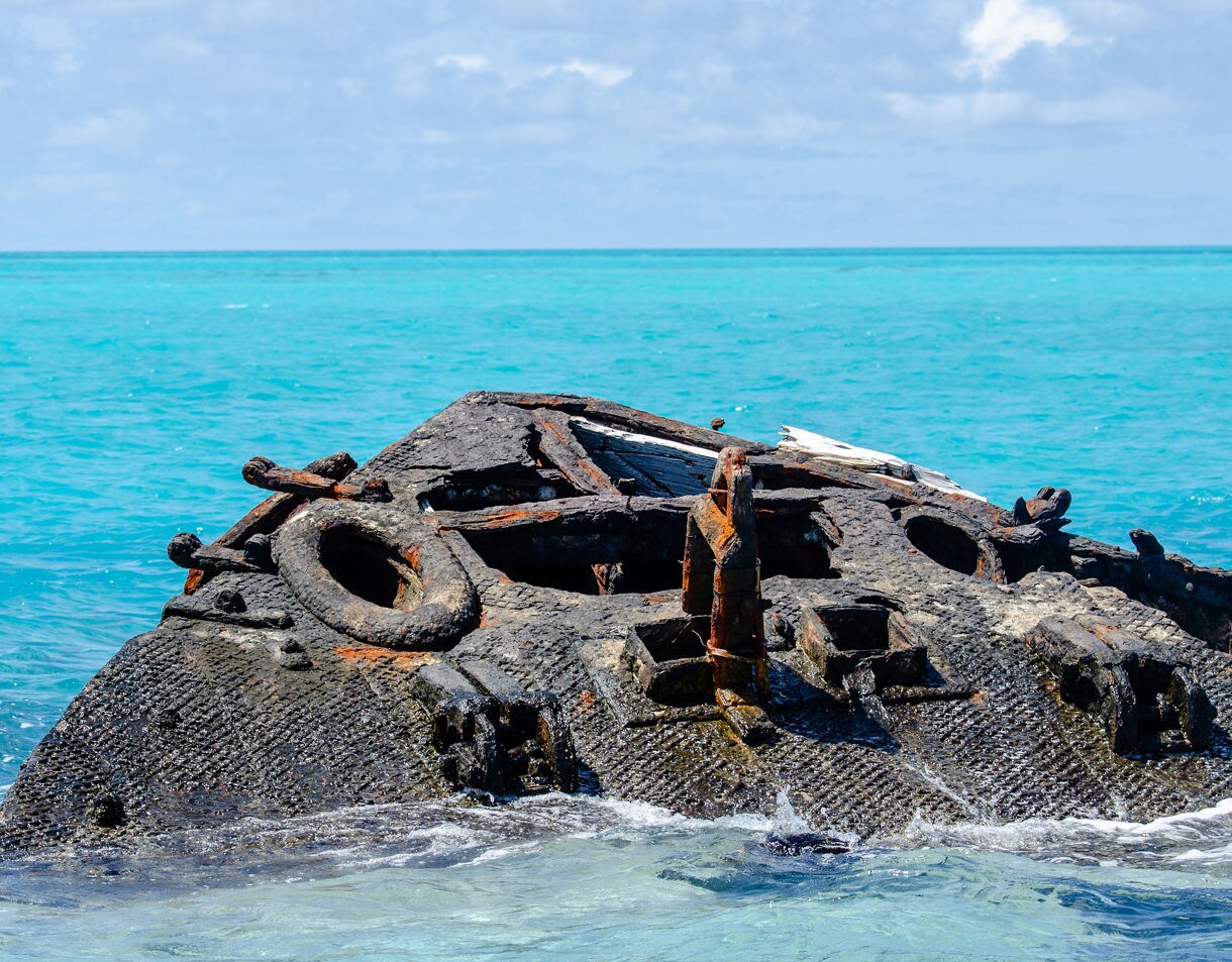 Rusted remains of the Vixen shipwreck partially submerged in turquoise ocean waters under a cloudy sky.