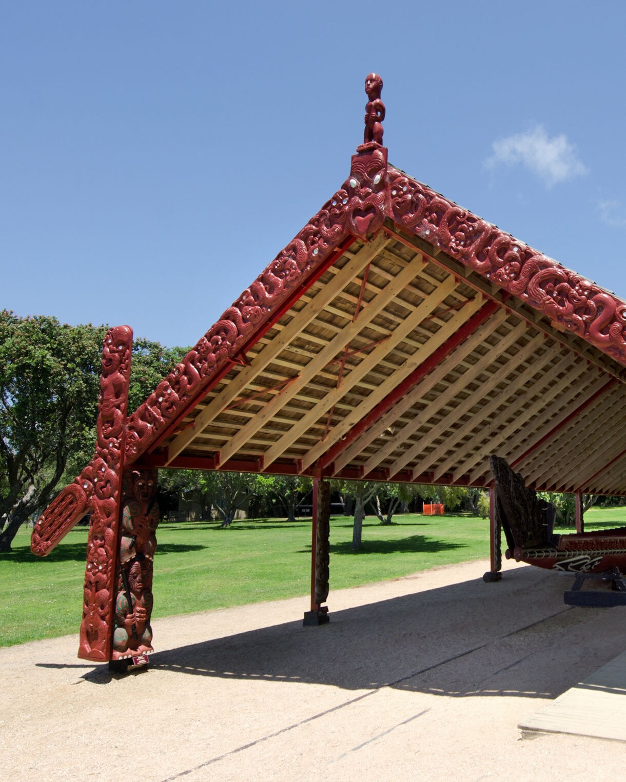 Traditional Māori meeting house with intricate red carvings and a ceremonial war canoe on display at the Waitangi Treaty Grounds in New Zealand.