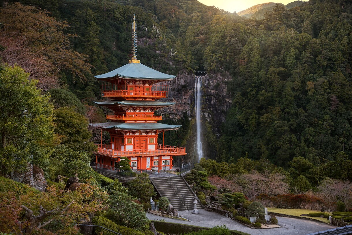 Vibrant red pagoda at Nachi Taisha with a tall waterfall cascading down a forested cliff in Wakayama.