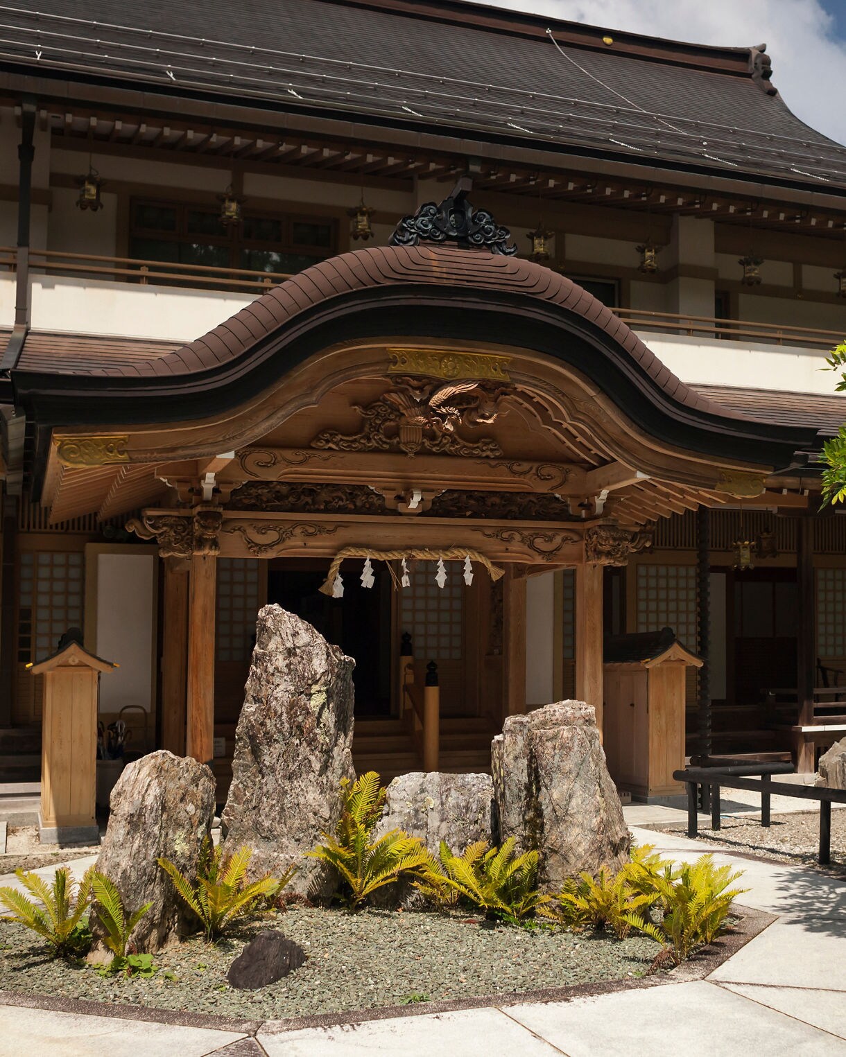 Traditional wooden monastery entrance with ornate carvings and a small rock garden in Koyasan, Japan.