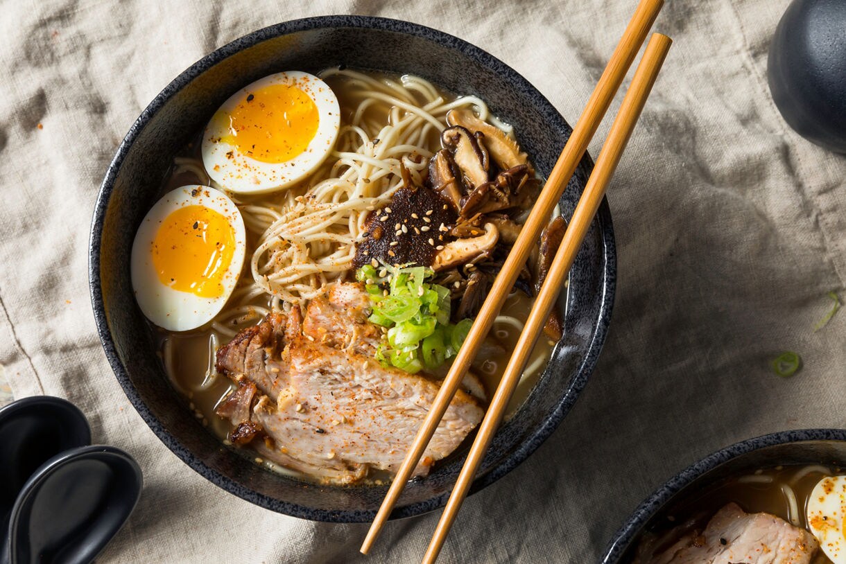 Bowl of ramen with soft-boiled eggs, sliced pork, mushrooms, green onions and chopsticks resting on top.