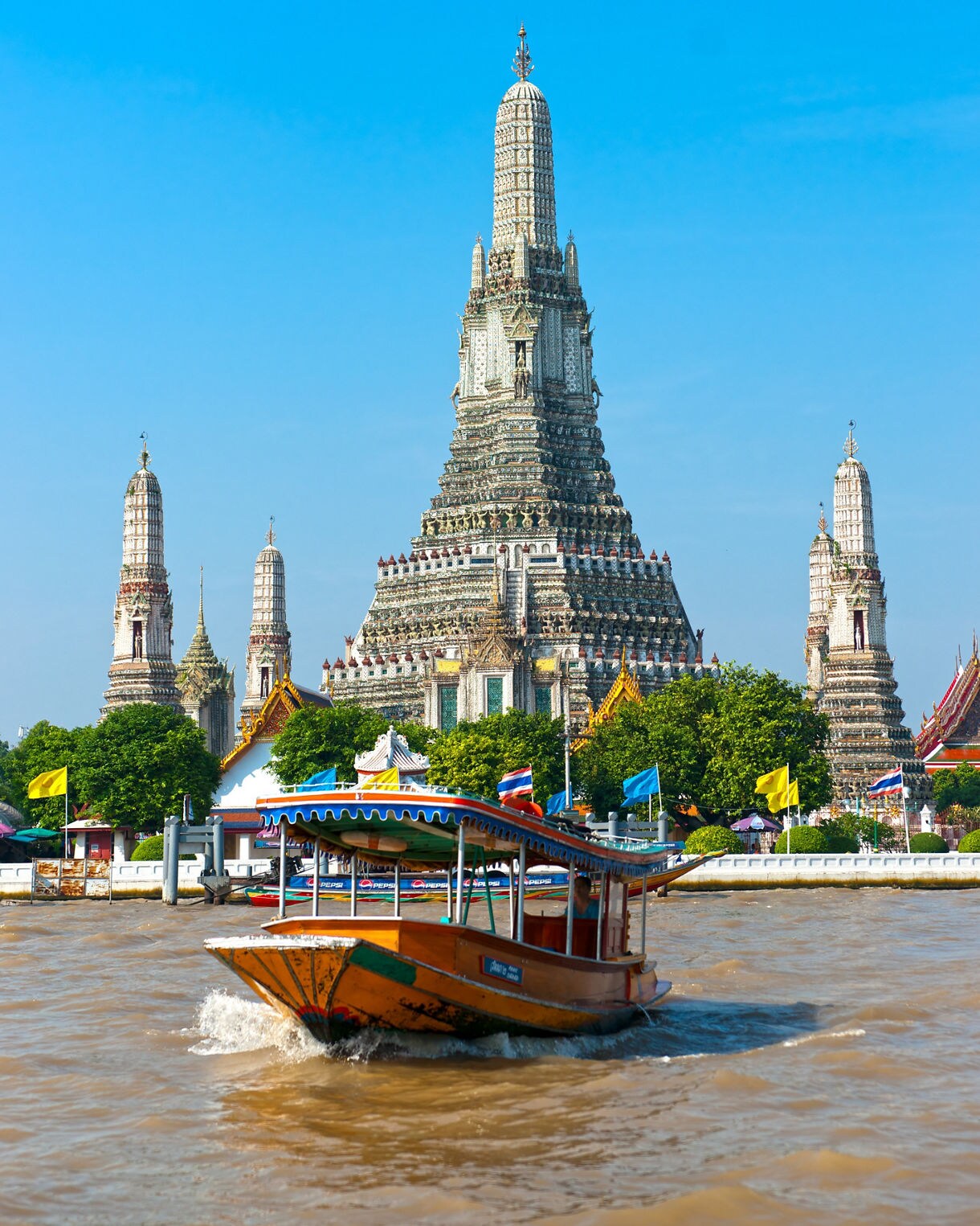 A colorful boat gliding on the Chao Phraya River with Wat Arun’s ornate central spire rising in the background.