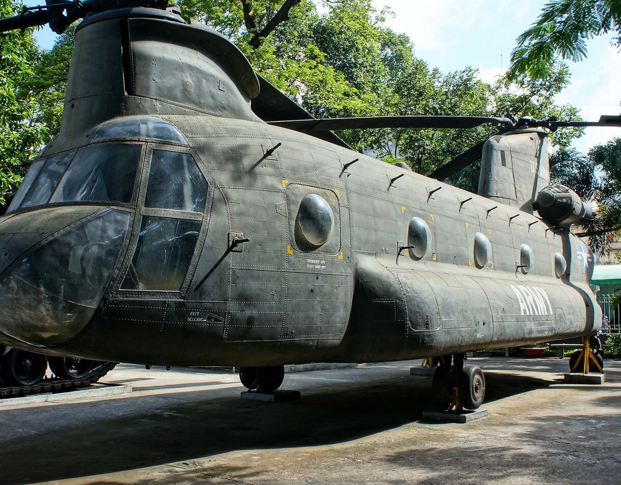 Restored military helicopter on display at the War Remnants Museum in Ho Chi Minh City, surrounded by trees and sunlight.