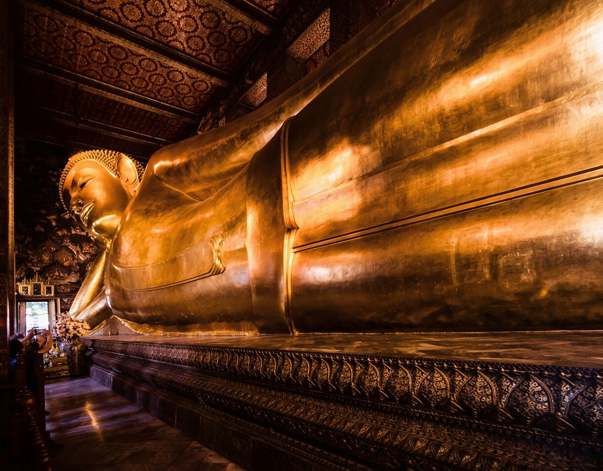 Massive golden Reclining Buddha statue inside Wat Pho temple in Bangkok, gleaming under ornate patterned ceilings and walls.
