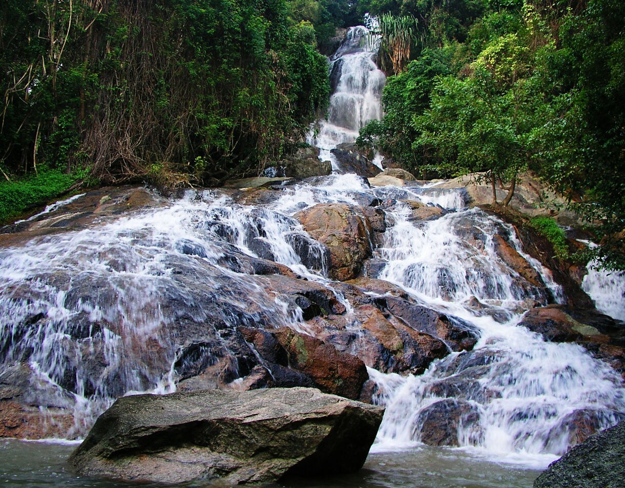 Multi-tiered Na Muang Waterfall flowing over smooth rocks surrounded by dense green forest in Koh Samui.