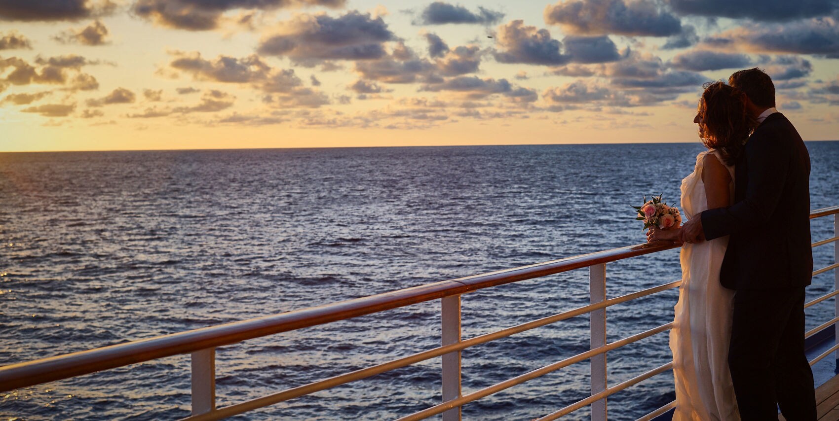 Couple embracing on deck while watching the sunset.