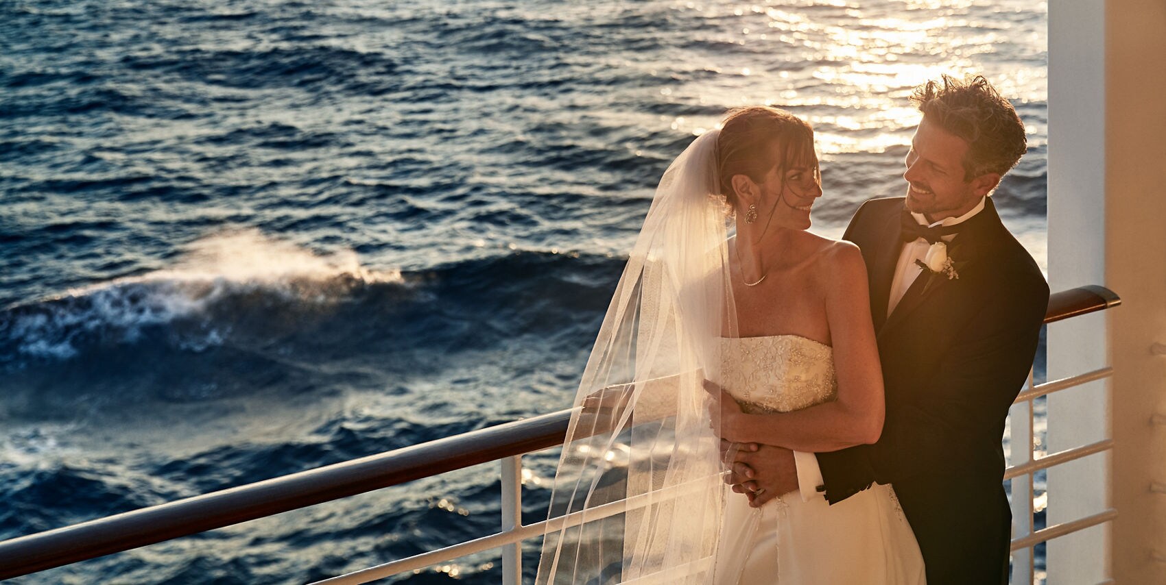 Bride and groom dressed in wedding attire, embracing on deck