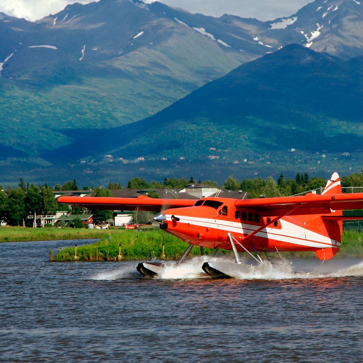 Bright orange seaplane taking off from Lake Hood in Anchorage, Alaska.