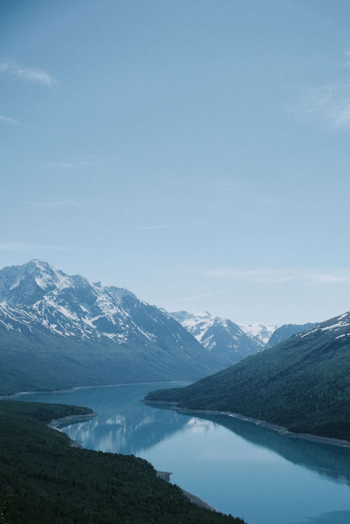 Aerial view of Eklutna Lake in Alaska, surrounded by forested valleys and snow-covered mountain ranges.