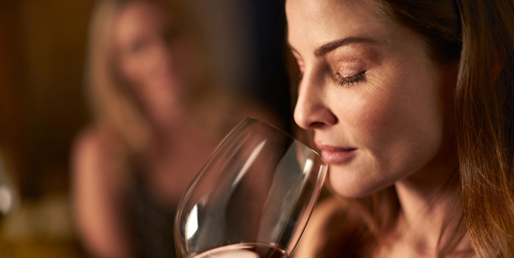 A woman closes her eyes and inhales the aroma of a glass of rosé wine.