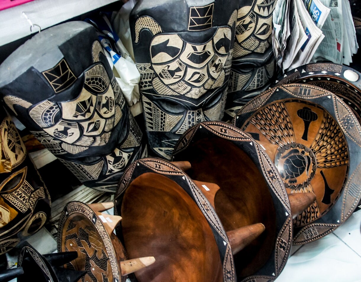 Close-up of traditional wooden Fijian carvings and kava bowls decorated with intricate geometric patterns, displayed together in a market setting.