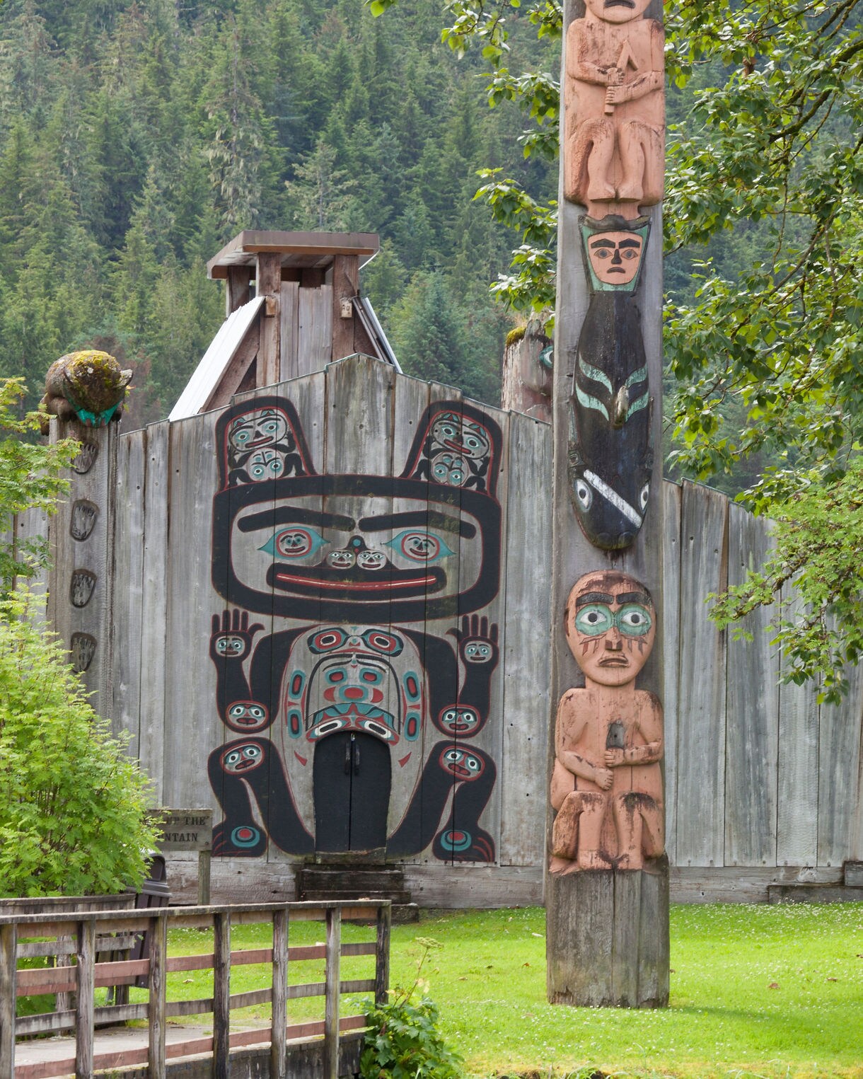 Tlingit clan house with totem pole and painted bear design, surrounded by trees in Wrangell, Alaska.