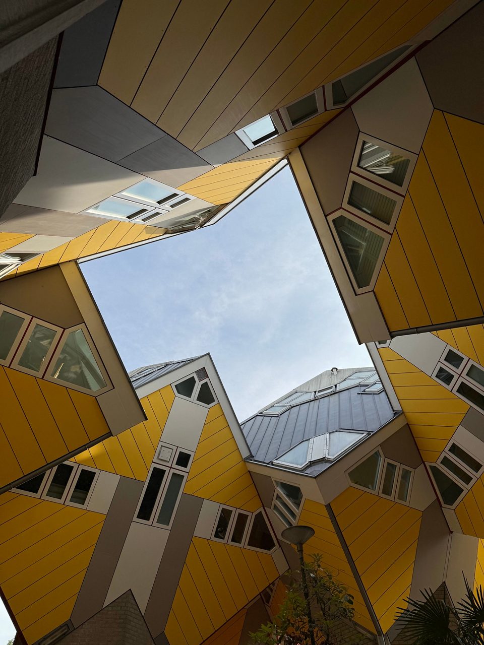 Upward view of Rotterdam’s yellow Cube Houses creating geometric shapes with windows and slanted walls against the sky.