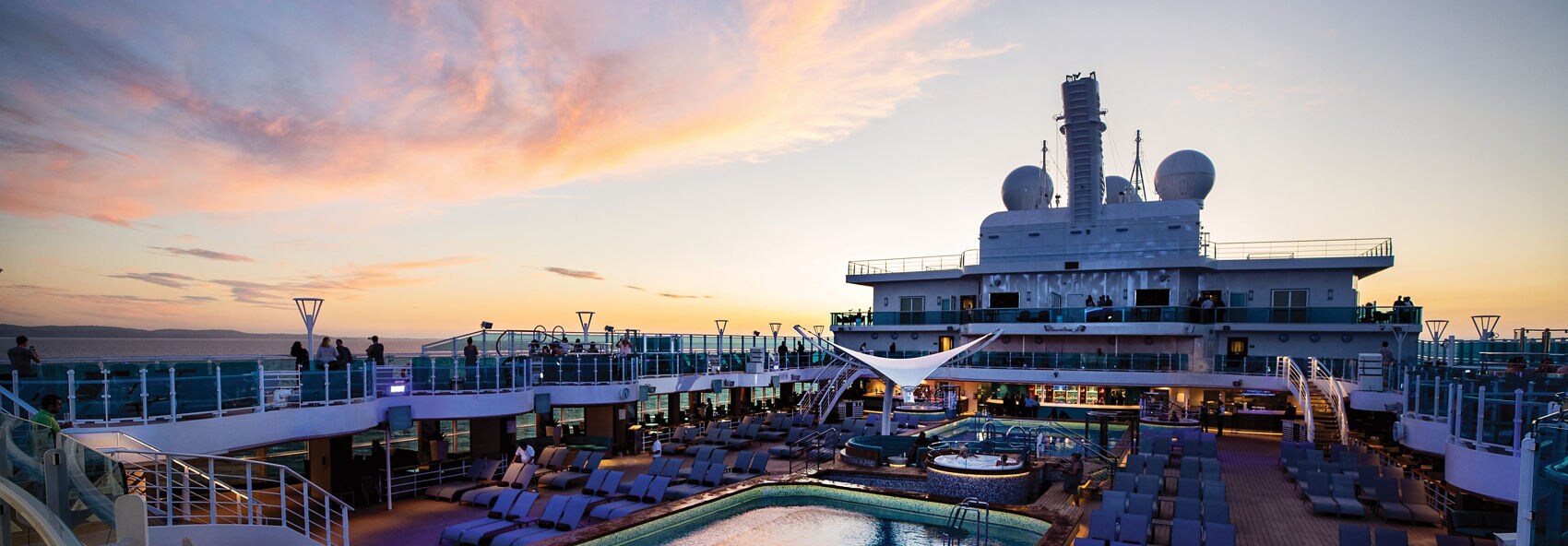  A cruise ship sets sail at sunset, with the ocean reflecting the warm golden hues of the sky. Passengers are seen on the deck enjoying the peaceful view as the ship glides across the water.