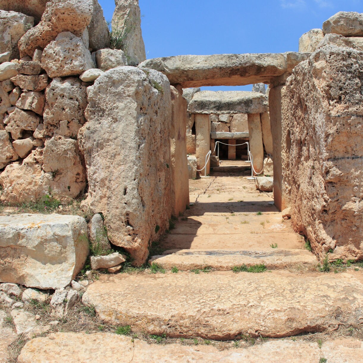 Entrance of Ħaġar Qim Temple in Malta, showing massive weathered limestone blocks forming a prehistoric doorway under a clear blue sky.